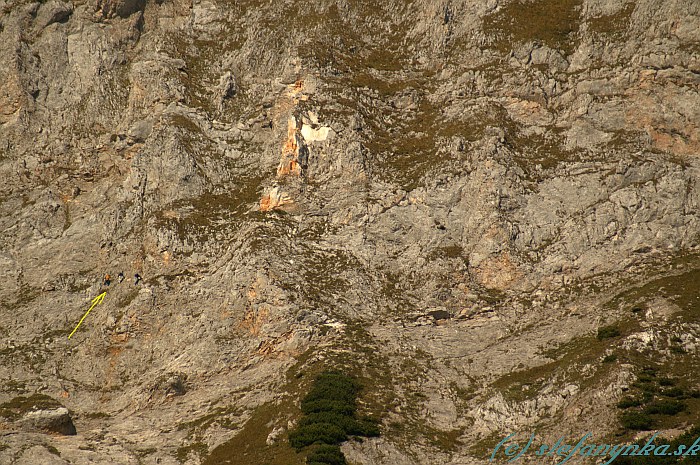 Ferrata Bismarck Steig pod strmými stenami Predigtstuhlu. Žltá šipka vľavo označuje trojicu feratistov