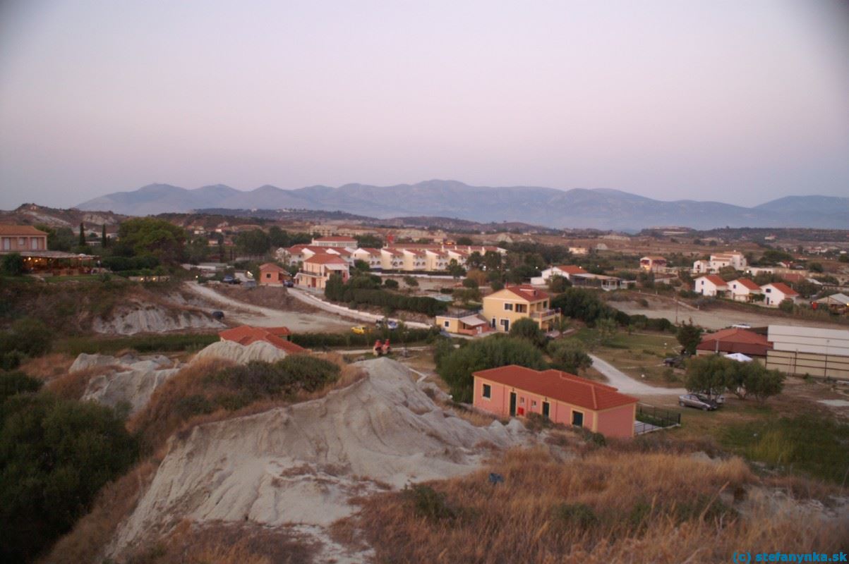 Lixouri-Xi, Kefalónia. Pohľad z útesov. V pravej časti je plážová taverna (svetlý vlnitý plech), mierne naľavo od stredu je trakt hotela Kefalonia palace