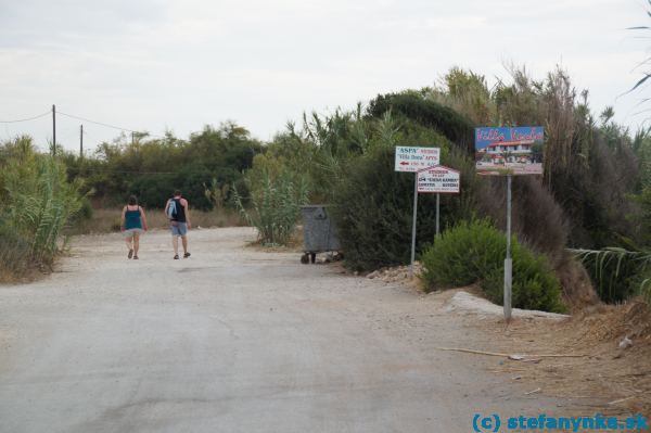 Z Agios Georgiosu vedie asfaltová cesta na juh popri pláži. Za tavernou Malibu asi po dvoch kilometroch končí asfaltka (pri týchto tabuliach). Ďalej je potrebné ísť rovno po poľnej ceste.