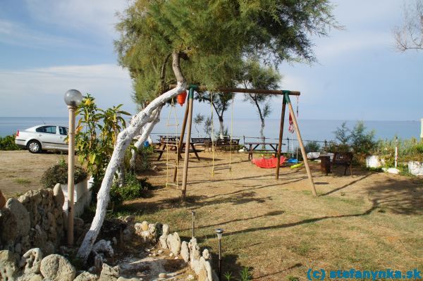 Parkovisko a detské ihrisko nad plážou Alex v južnej časti Agios Georgios south, neďaleko od taverny Malibu
